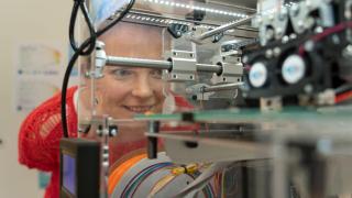 Nainen katsoo lumoutuneena 3D-tulostinta.